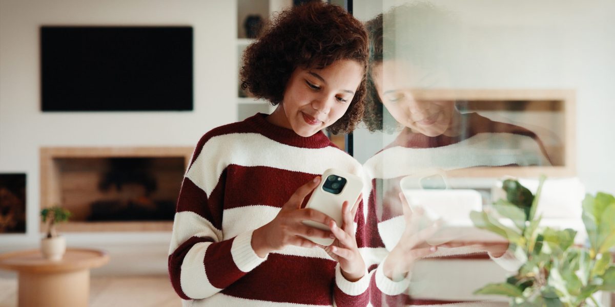 Phone, smile and window with teen girl in home living room for social media or text message. App, reflection in glass and typing with kid in apartment for connection, internet browsing or search.