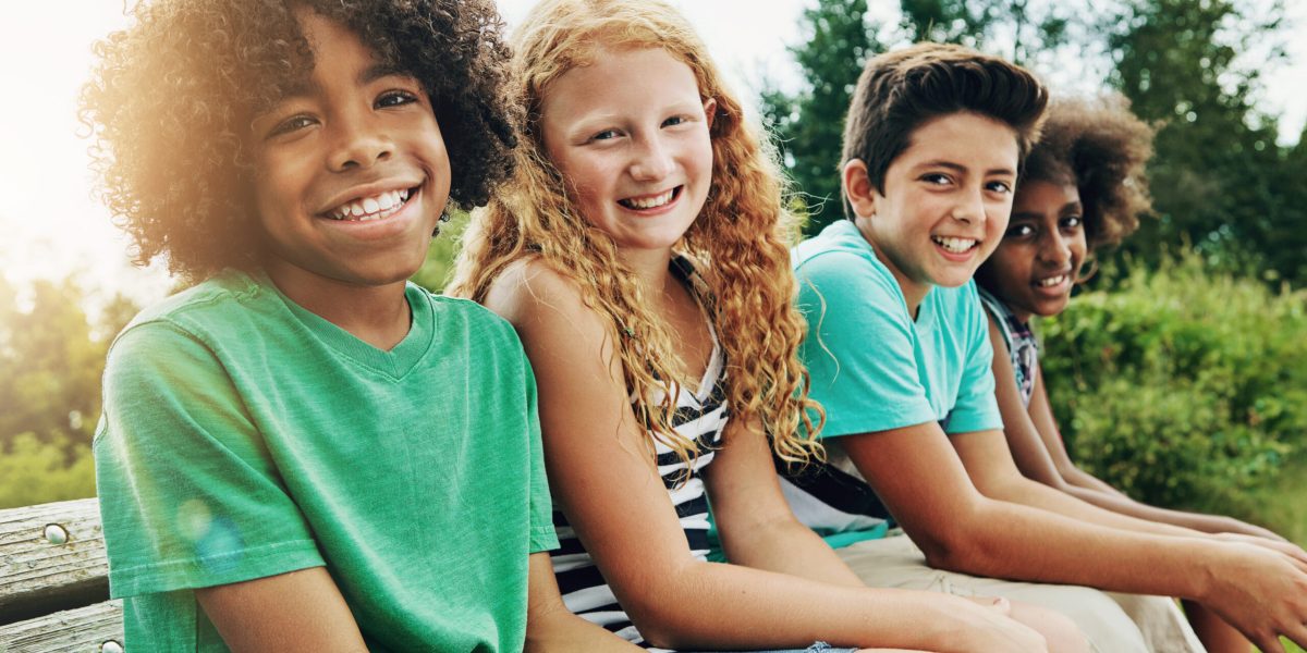 Portrait, outdoor and children on bench, smile and diversity with fun, summer and weekend break. Face, group and kids in park, nature and bonding together with friends, playful and cheerful with joy.